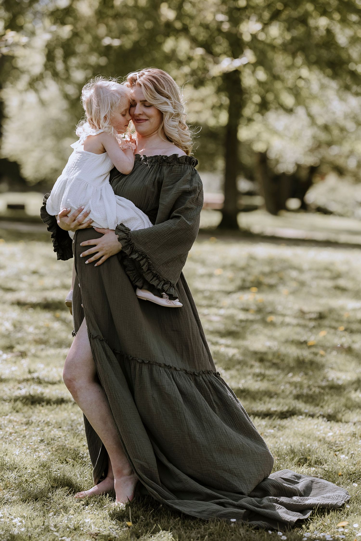 A tender moment captured outdoors shows an olive green maxi dress with bell sleeves against a sunlit garden backdrop.