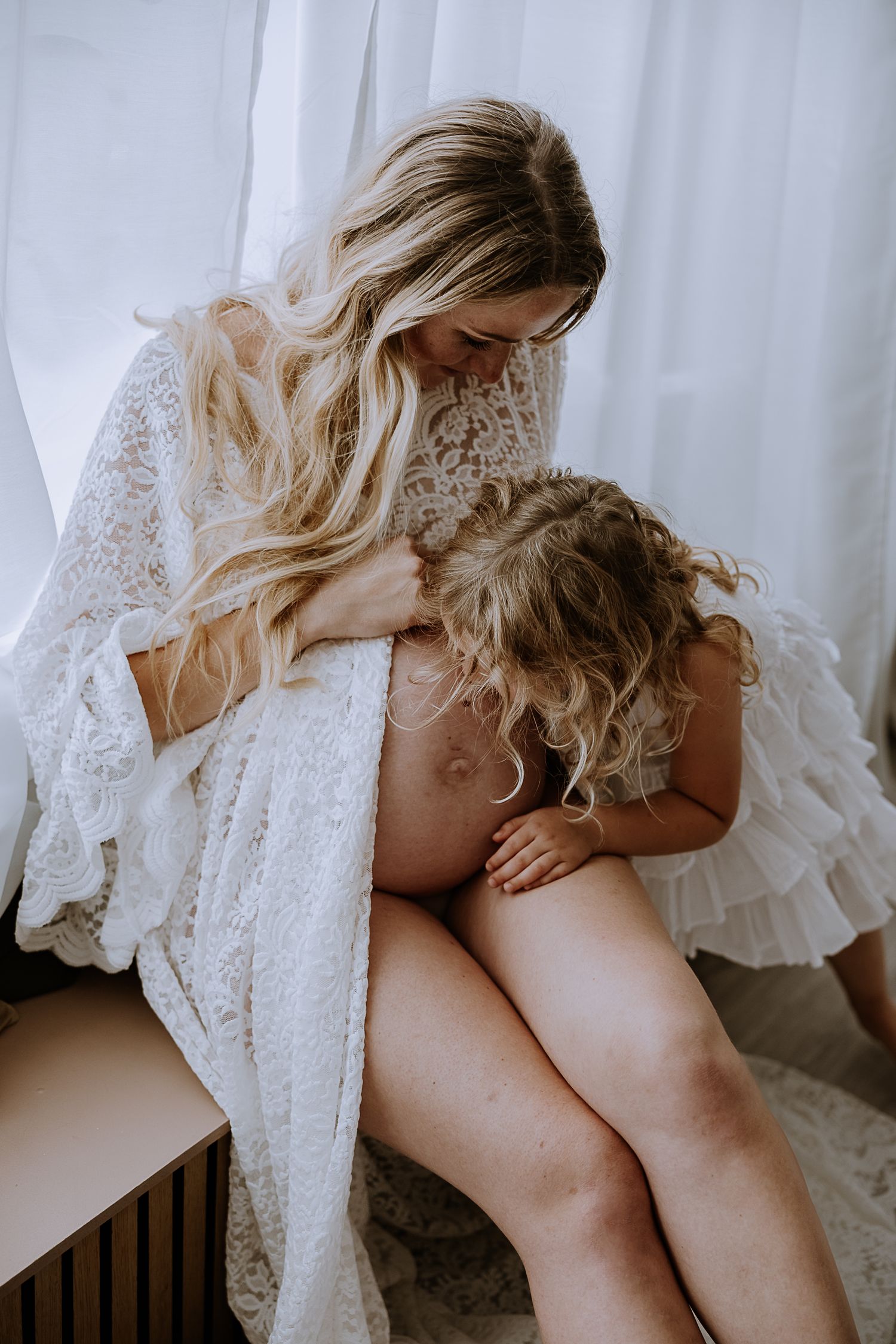 A tender moment captured in soft light shows an intimate portrait of family connection with delicate white lace details.
