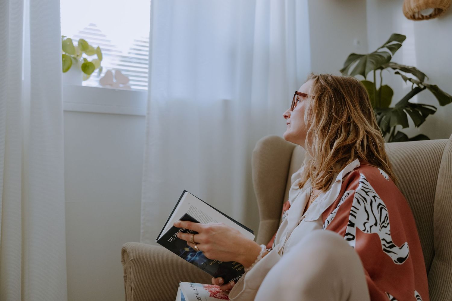 A person relaxes in a bright room with houseplants while reading a book.