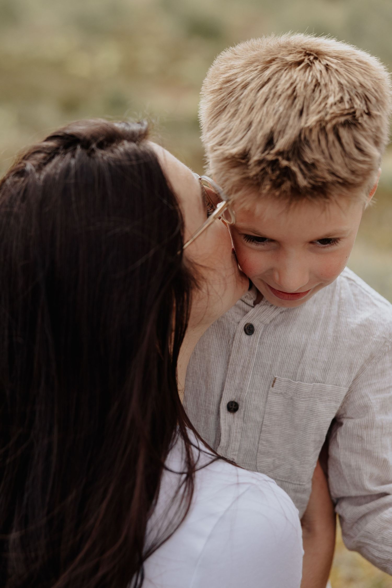 Intimate portrait of parent giving child a gentle kiss on the cheek outdoors.