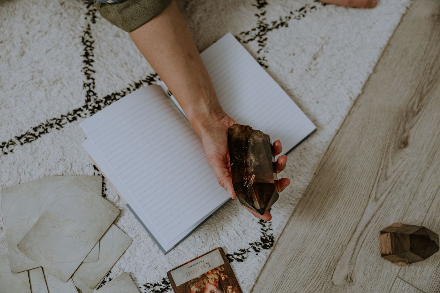 Hands writing in a notebook with crystals on a light wooden surface.