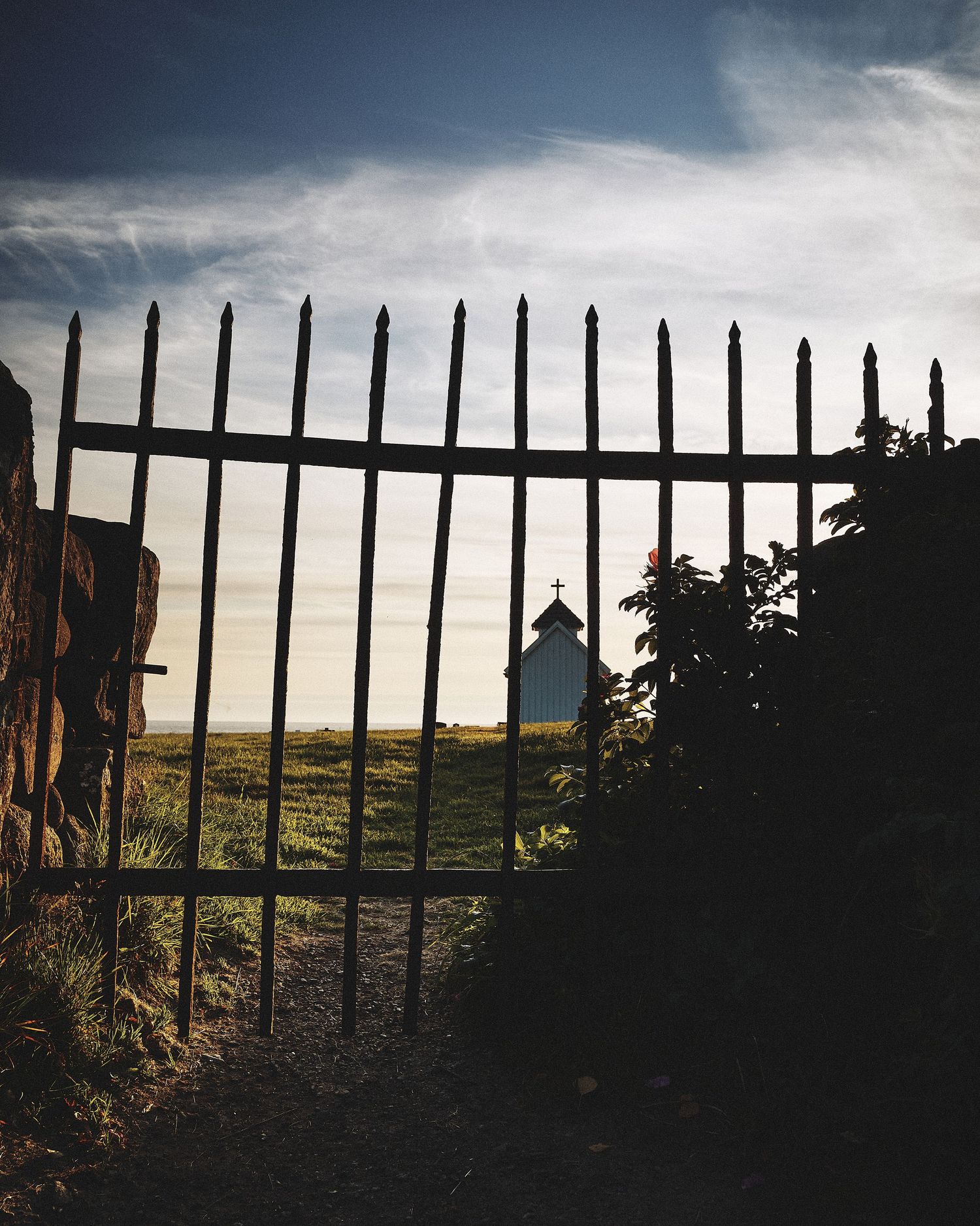 Dark silhouette of a wooden fence against a moody sky with grassy hills in the background.