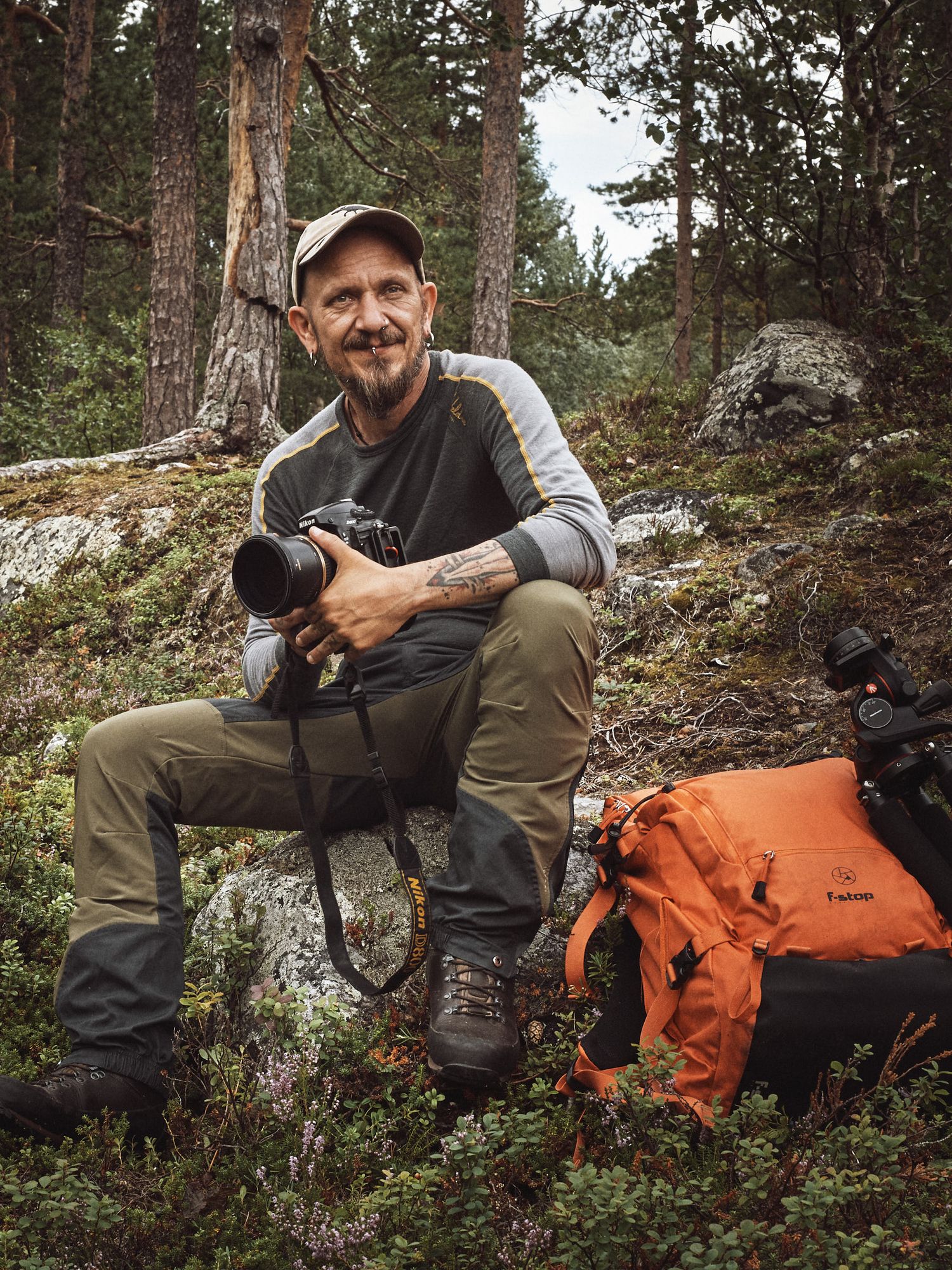 Wildlife photographer lying on ground in forest setting with camera and orange backpack capturing nature shots.