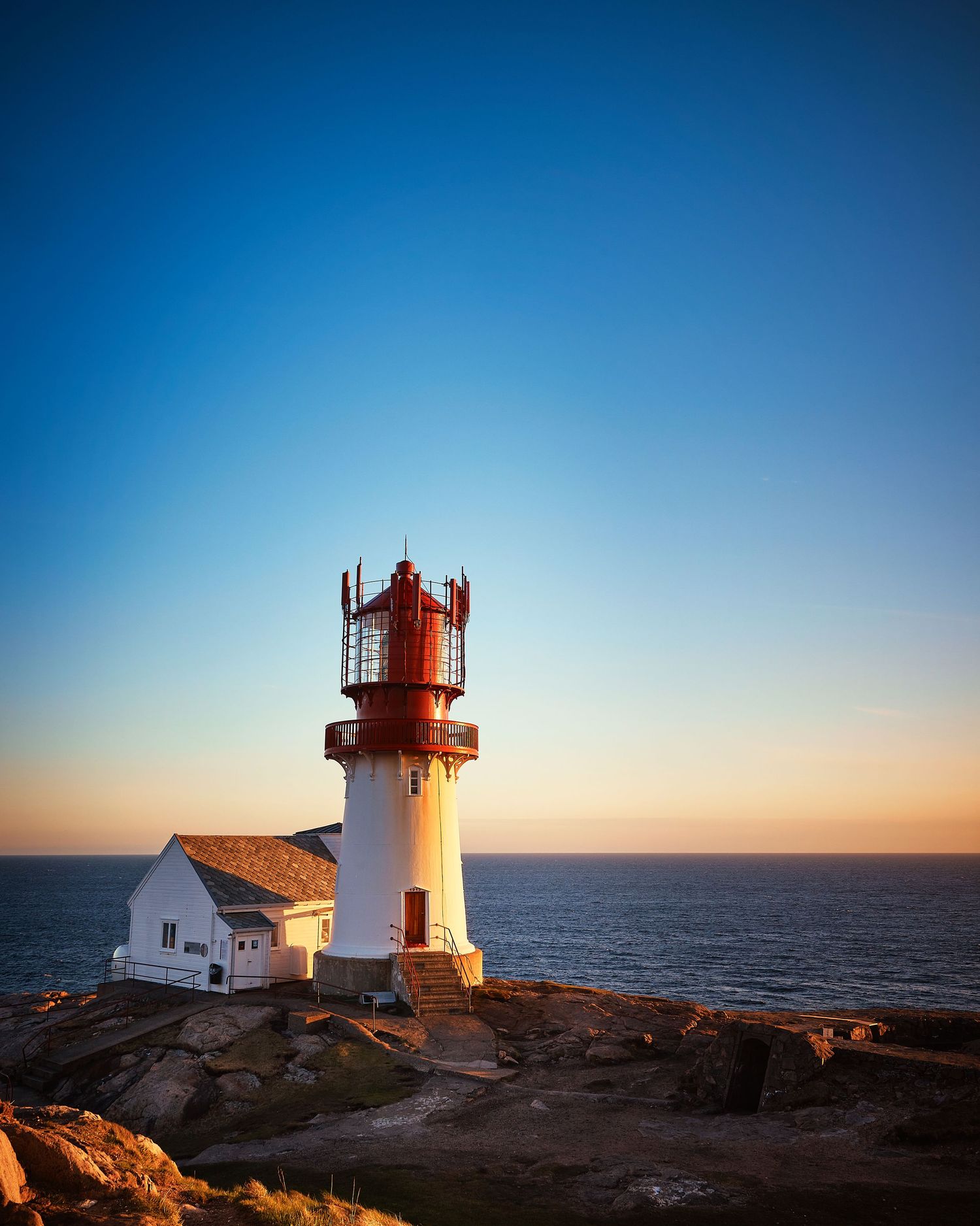 Lighthouse and keeper's house at sunset on rocky coastal point.