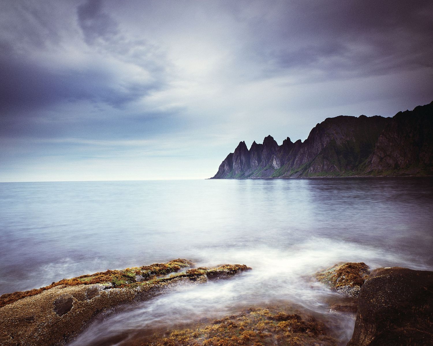 Long exposure seascape of jagged coastal cliffs in moody weather.