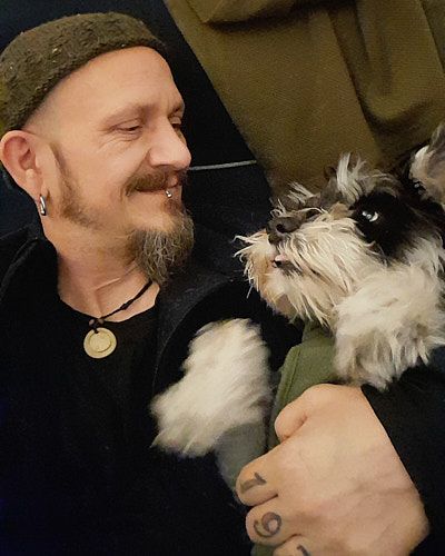 A white fluffy dog gives affectionate kisses to a person wearing black while being held in their arms.