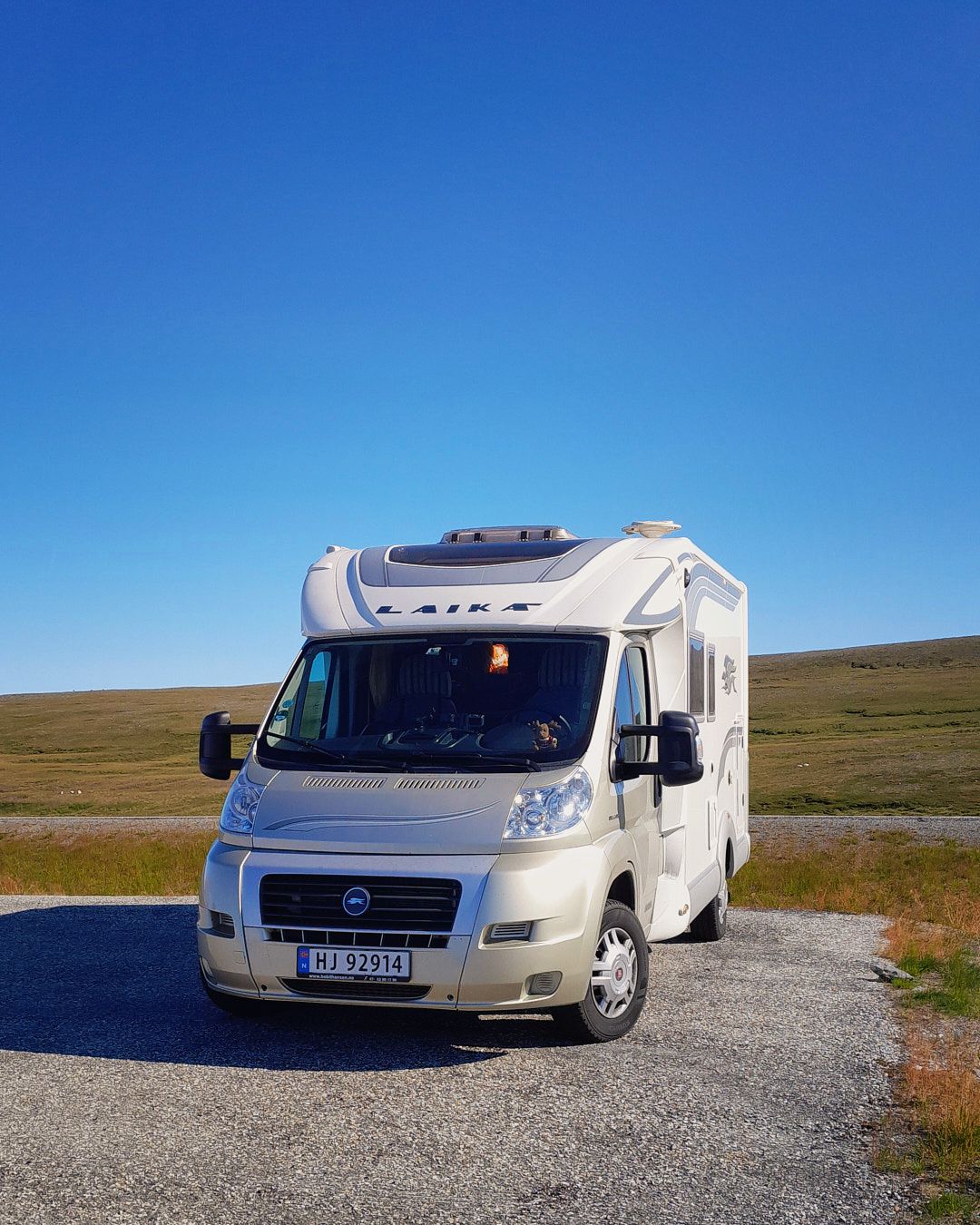 White motorhome parked on gravel road against backdrop of rolling hills and blue sky.