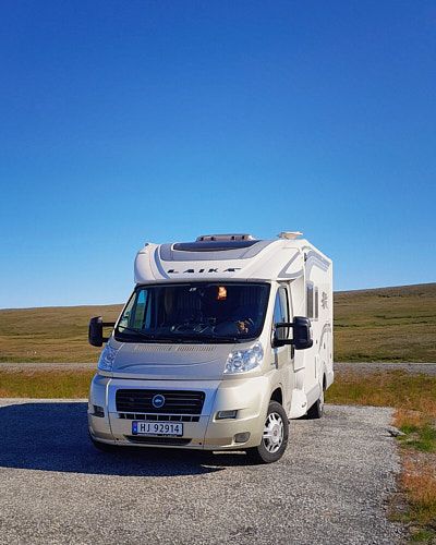 White motorhome camper van parked on gravel against scenic mountain landscape under bright blue sky.