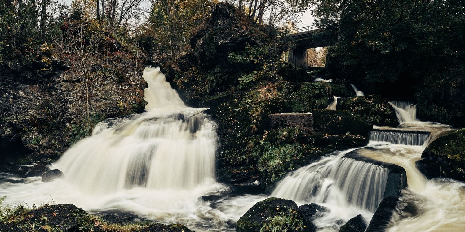 Wide waterfall cascades over multiple rocky ledges in a natural forest setting.