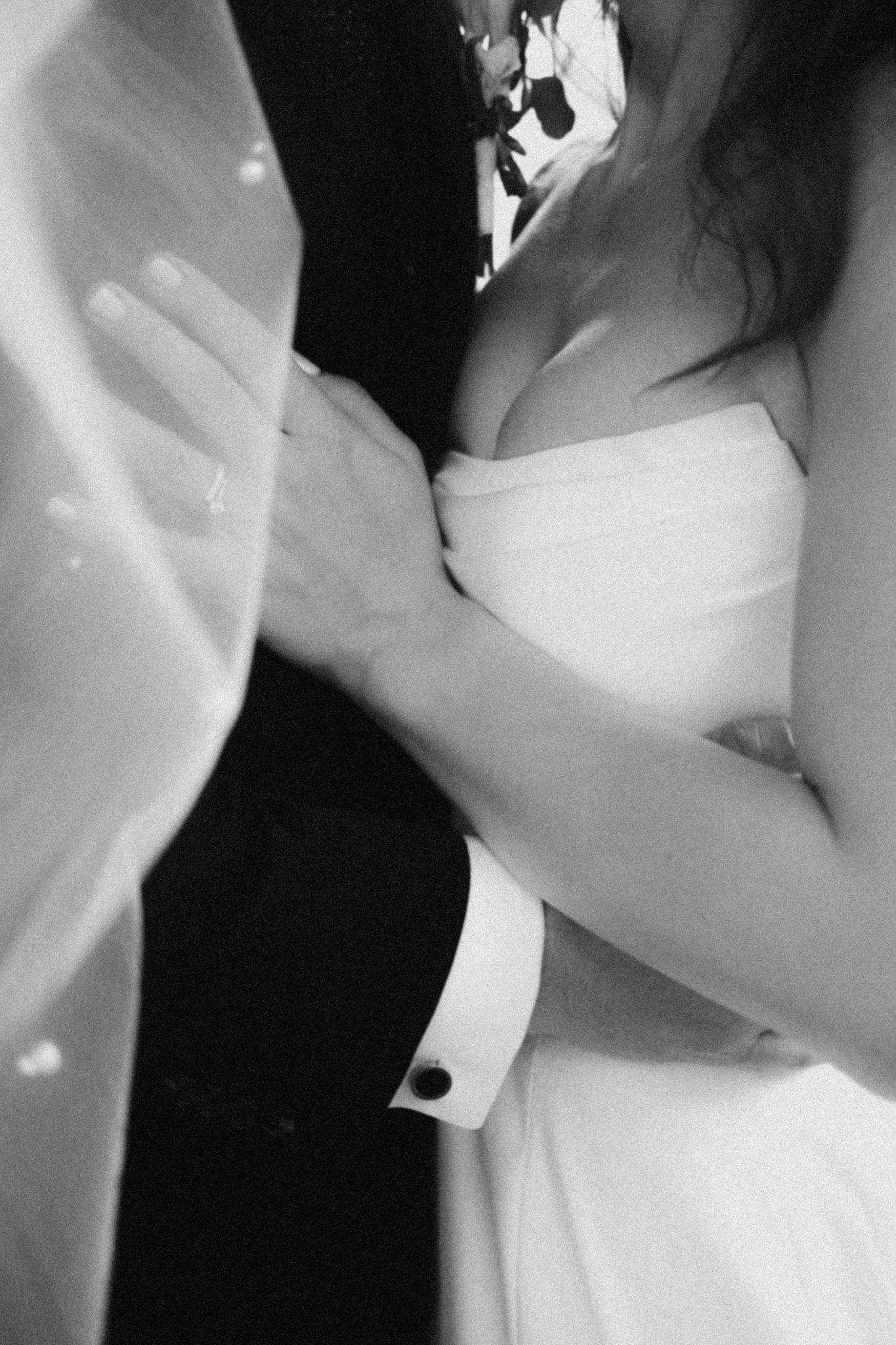Černobílá Svatební fotografie v detailním záběru zachycující intimní taneční objetí postav ve svatebním oblečení.