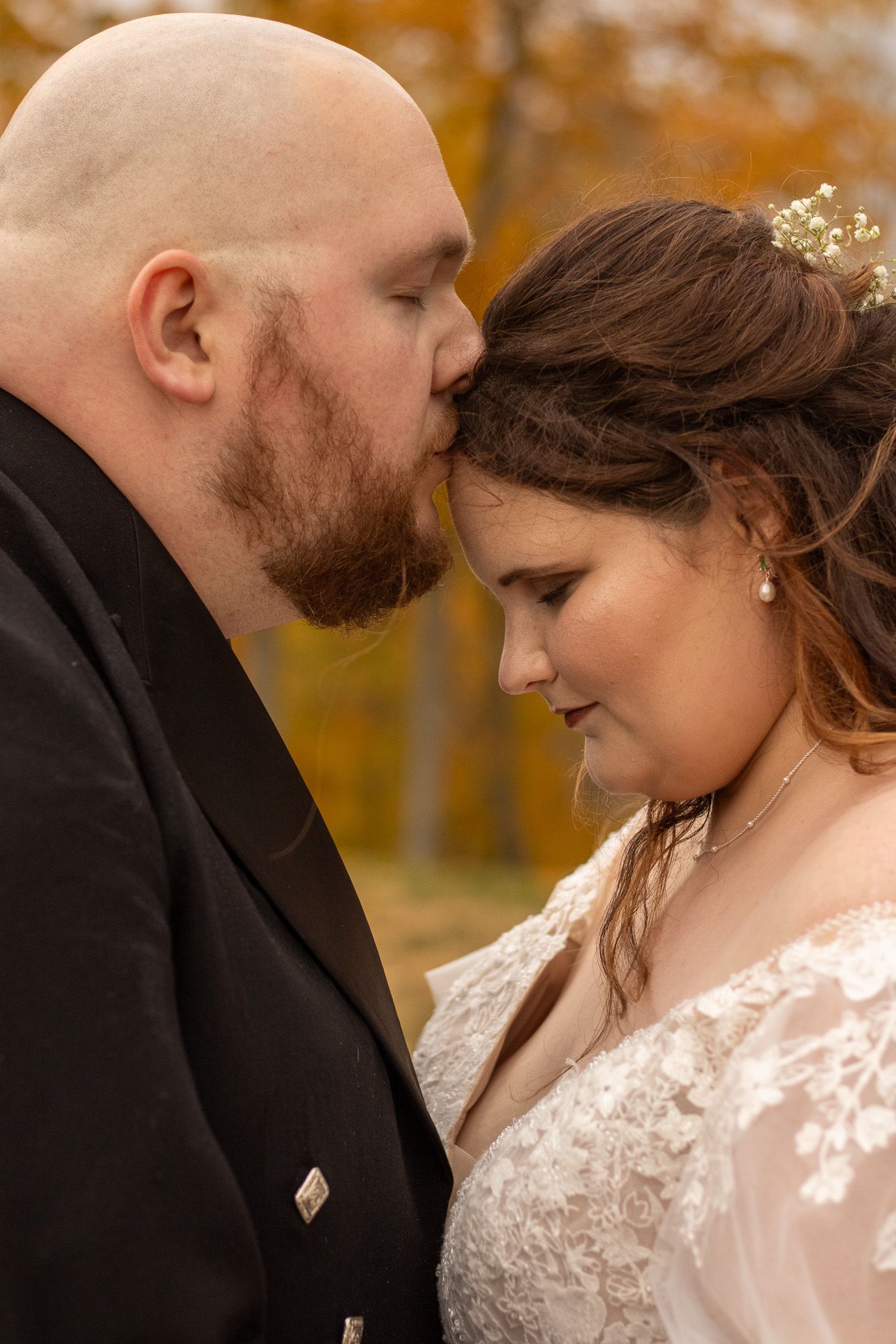 Intimate wedding portrait of newlyweds sharing a tender moment outdoors with autumn foliage in background.