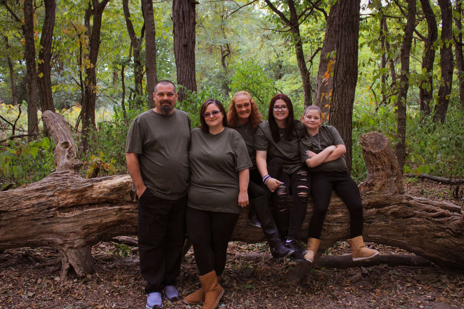 A group of people pose together on a large fallen tree trunk in a lush green forest setting.