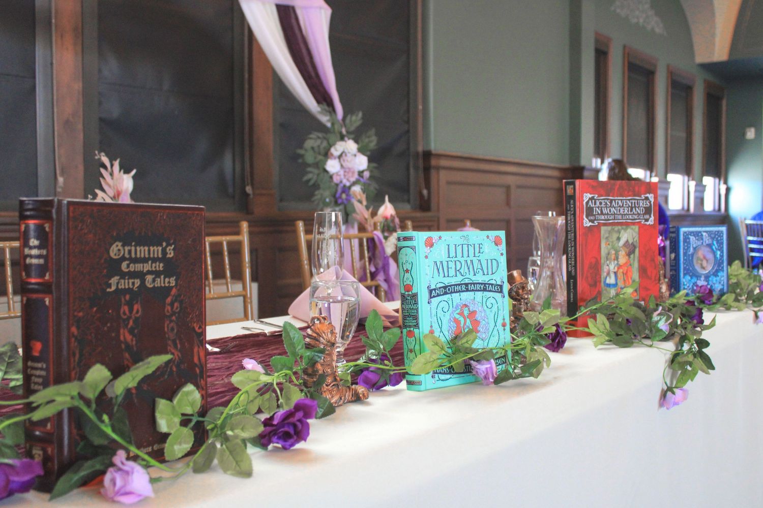 Colorful children's storybooks displayed on a table with purple flowers and green foliage decorations.