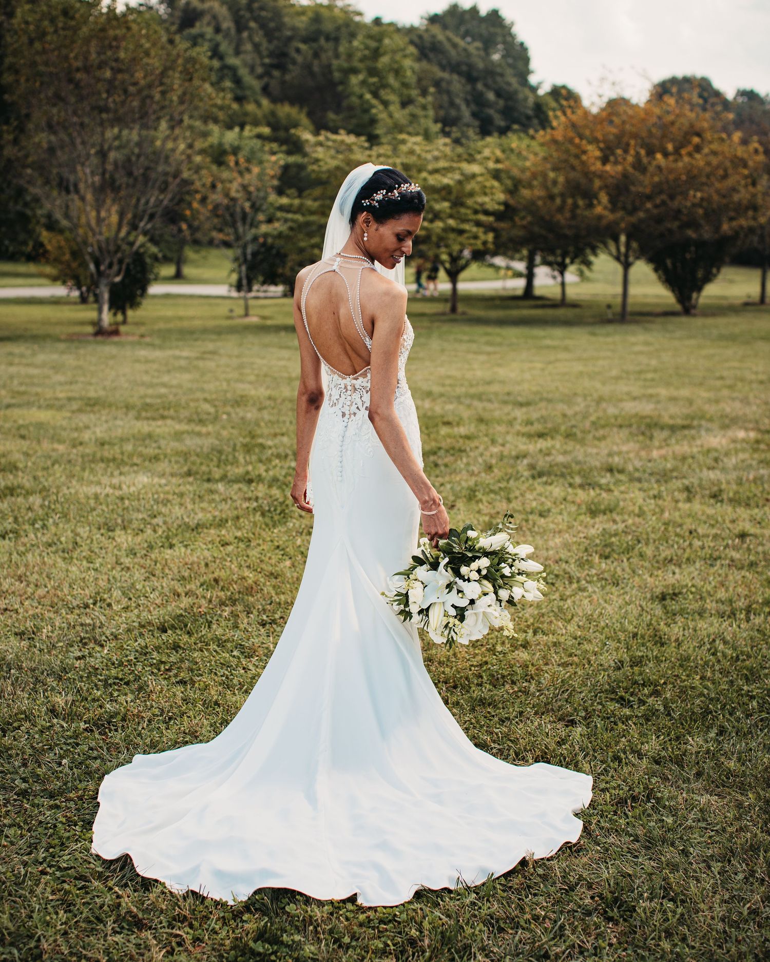 An elegant backless wedding dress with a flowing train photographed in a scenic outdoor setting during golden hour.