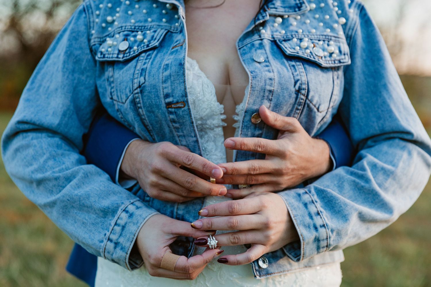 A detailed view of hands wearing rings against a denim jacket with pearl embellishments.
