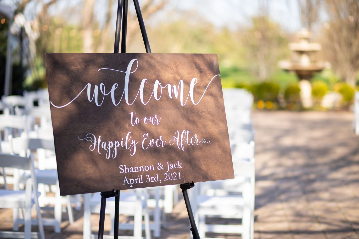 Wedding welcome sign with calligraphy text reading 'Welcome to our Happily Ever After' displayed on easel at outdoor venue.