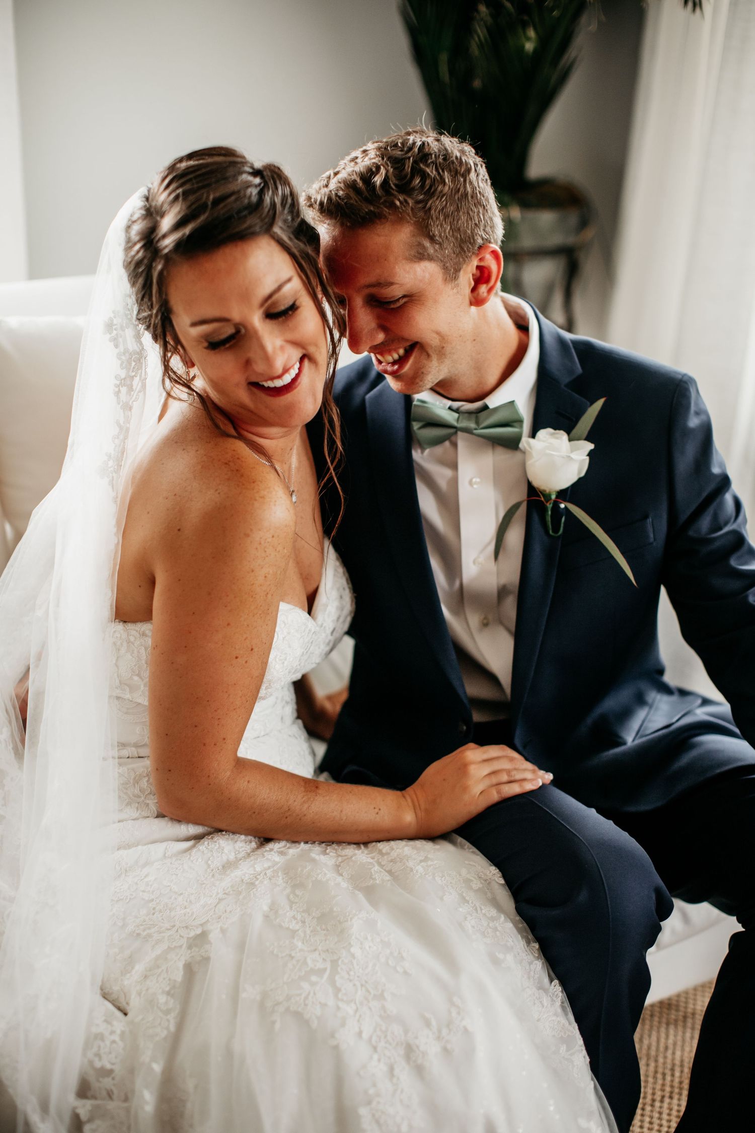 A joyful intimate moment of newlyweds laughing together, with bride in white dress and groom in navy suit with bowtie.
