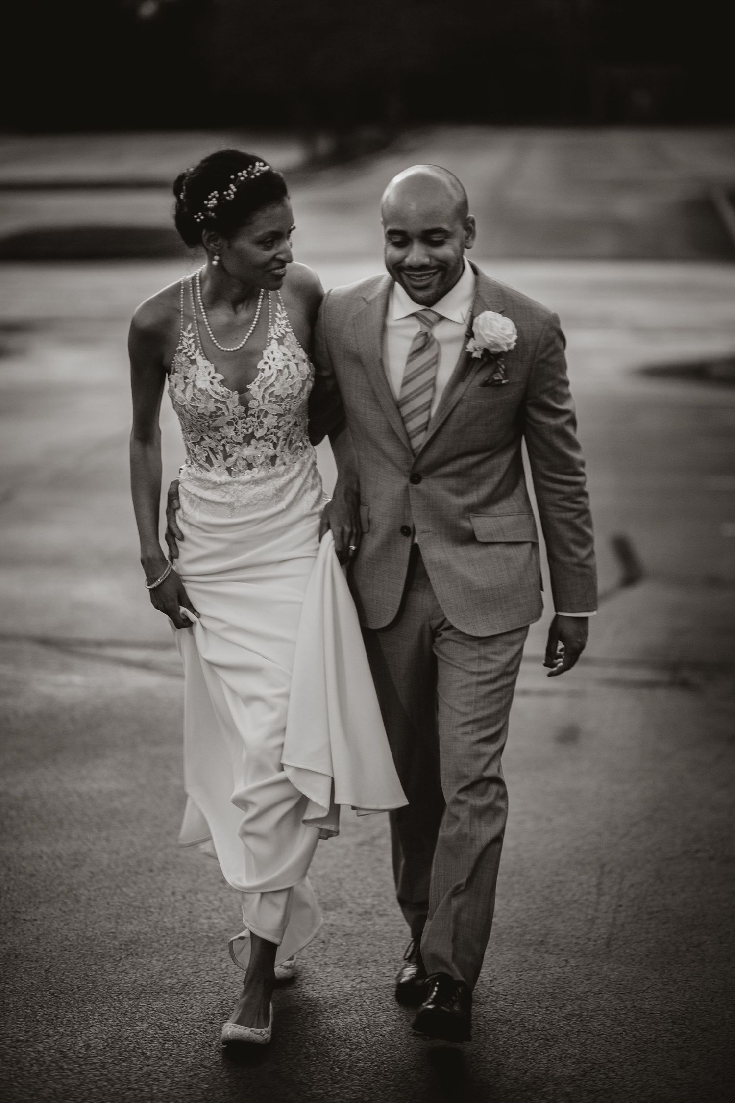 Romantic black and white photo of a couple walking together on their wedding day in elegant attire.