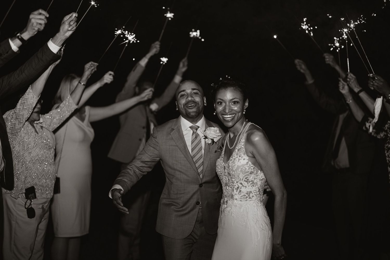 A wedding celebration during an evening reception with guests raising sparklers in the background.