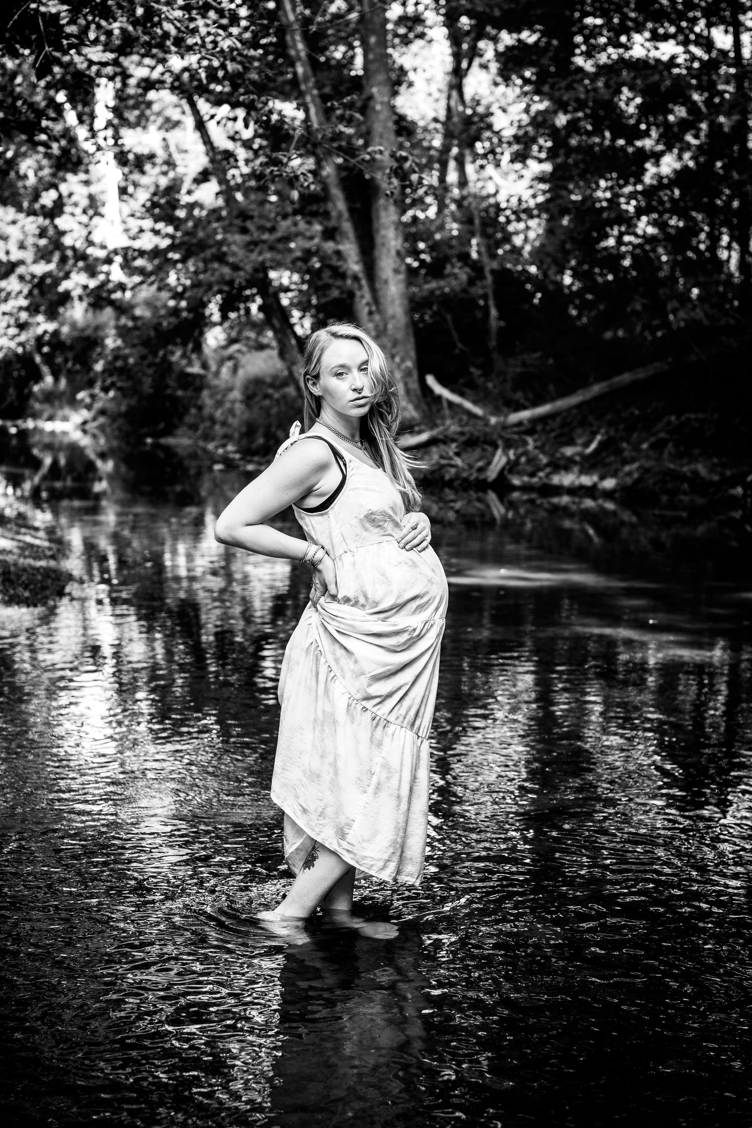 Artistic black and white maternity photo of an expectant mother standing in a stream.