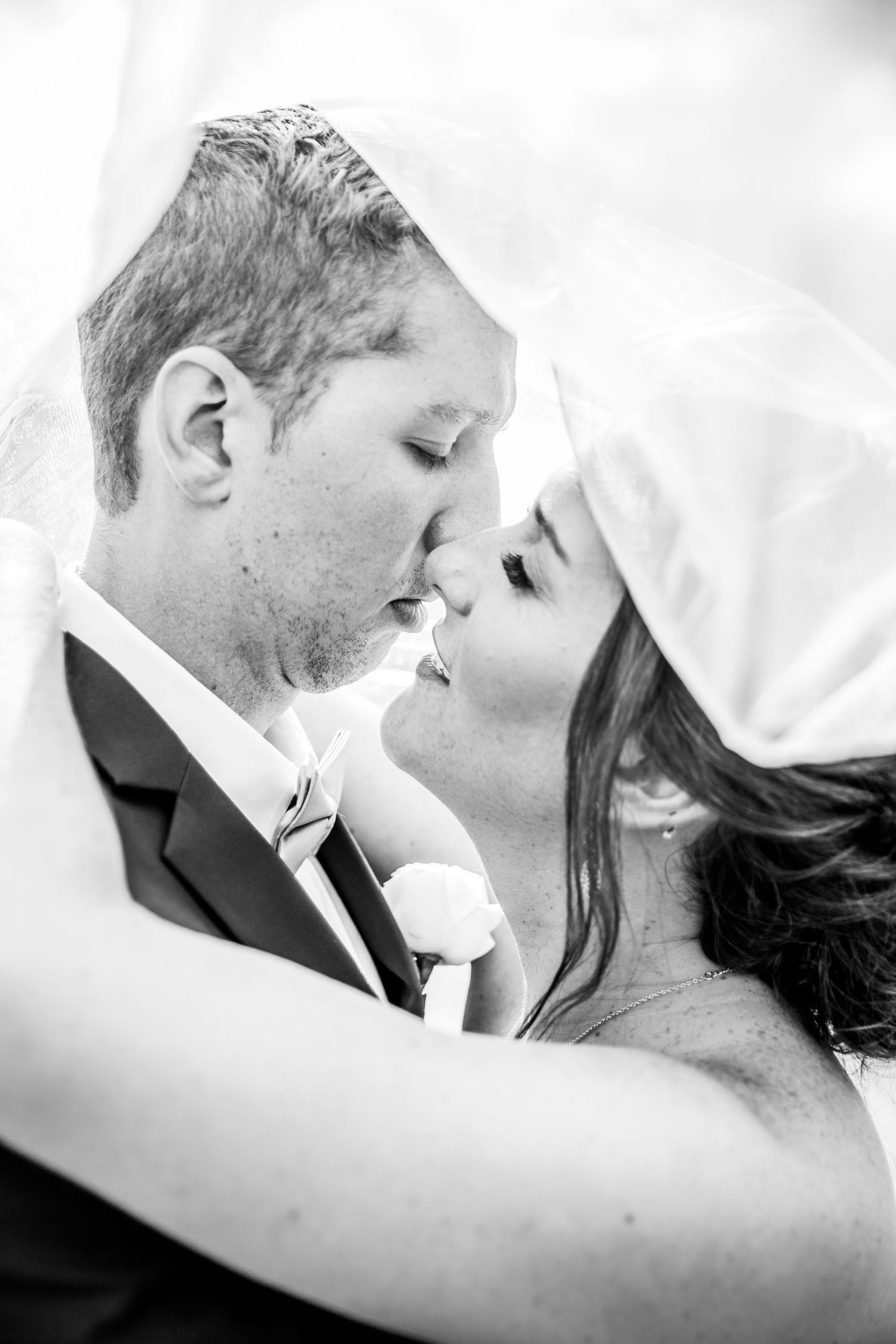Black and white romantic wedding photograph showing a tender intimate moment between newlyweds under a veil.