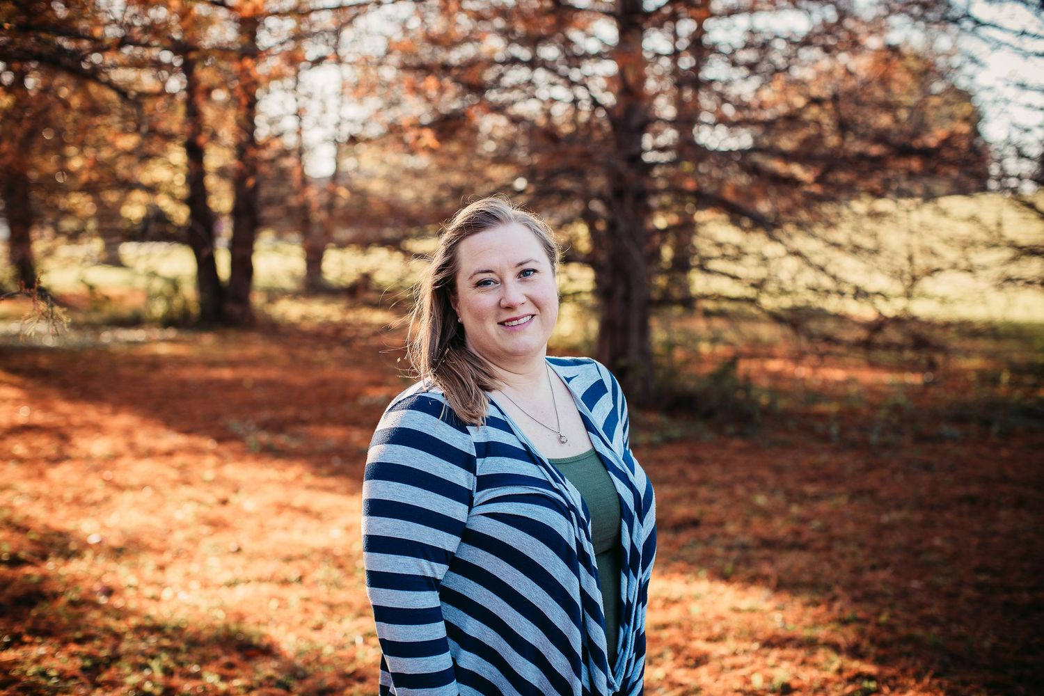 Person in striped shirt smiling in autumn forest setting.