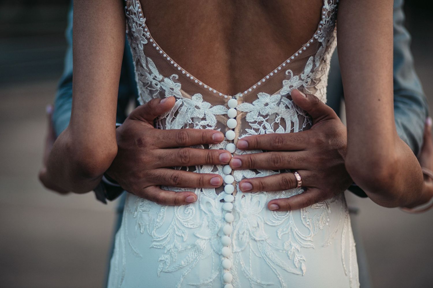 Close up detail shot of delicate lace wedding dress buttons and embellishments with hands on waist.