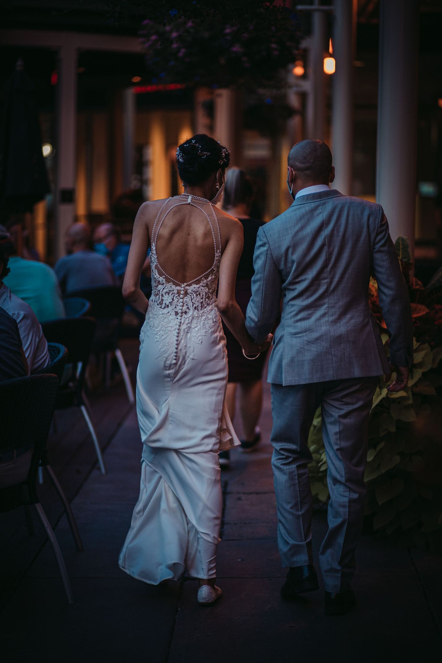 A romantic evening scene showing detailed back of white wedding gown as couple walks through venue.