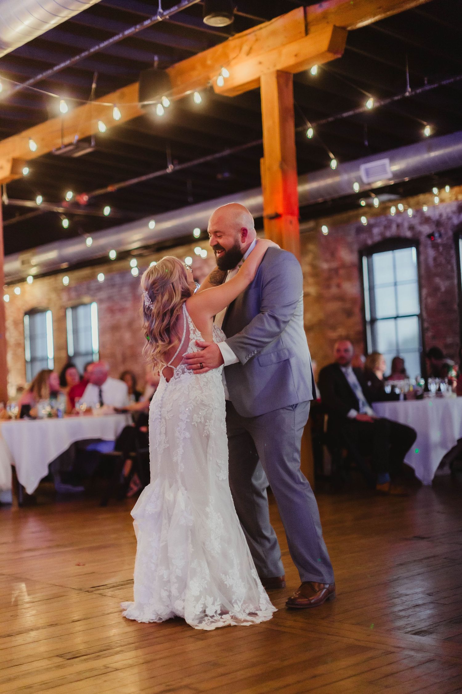 Romantic first dance at rustic wedding reception with exposed brick walls and string lights.
