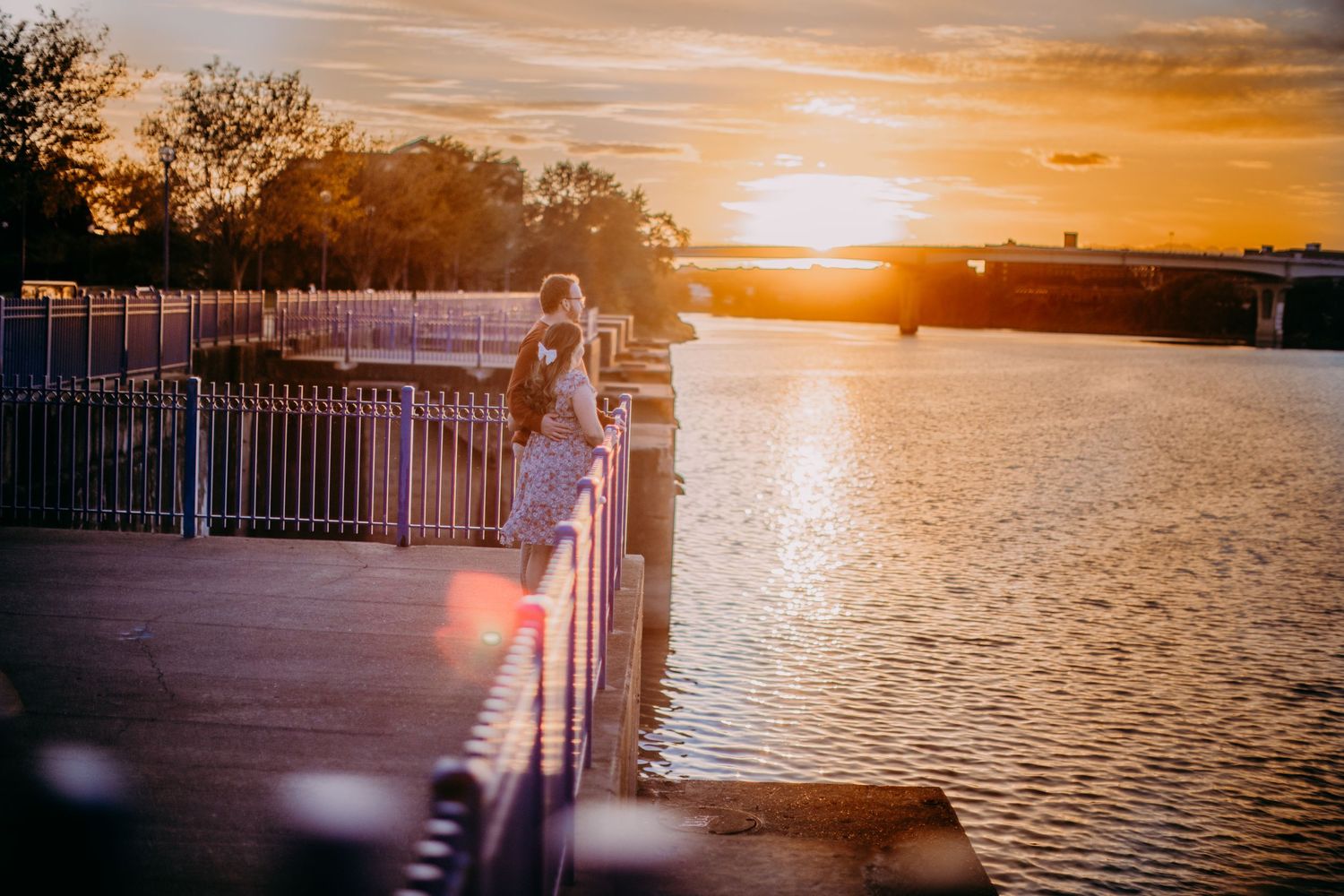 Beautiful sunset over a waterfront with metal railings creating silhouettes against the orange sky.
