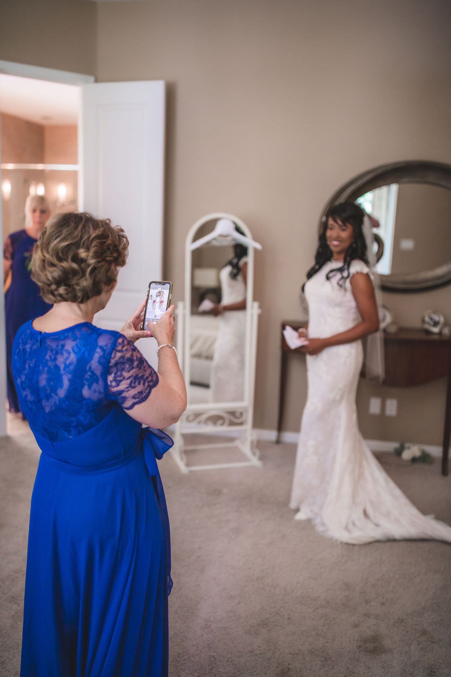 Bridesmaids in cobalt blue dresses assist with wedding preparations in a sunlit room.