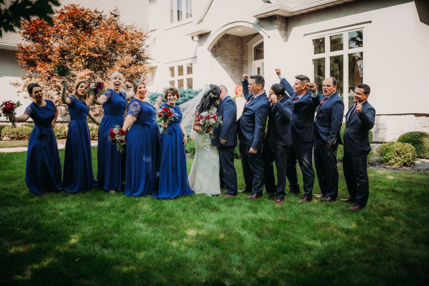 Wedding party in coordinated navy blue attire poses for formal group photo on mansion lawn.