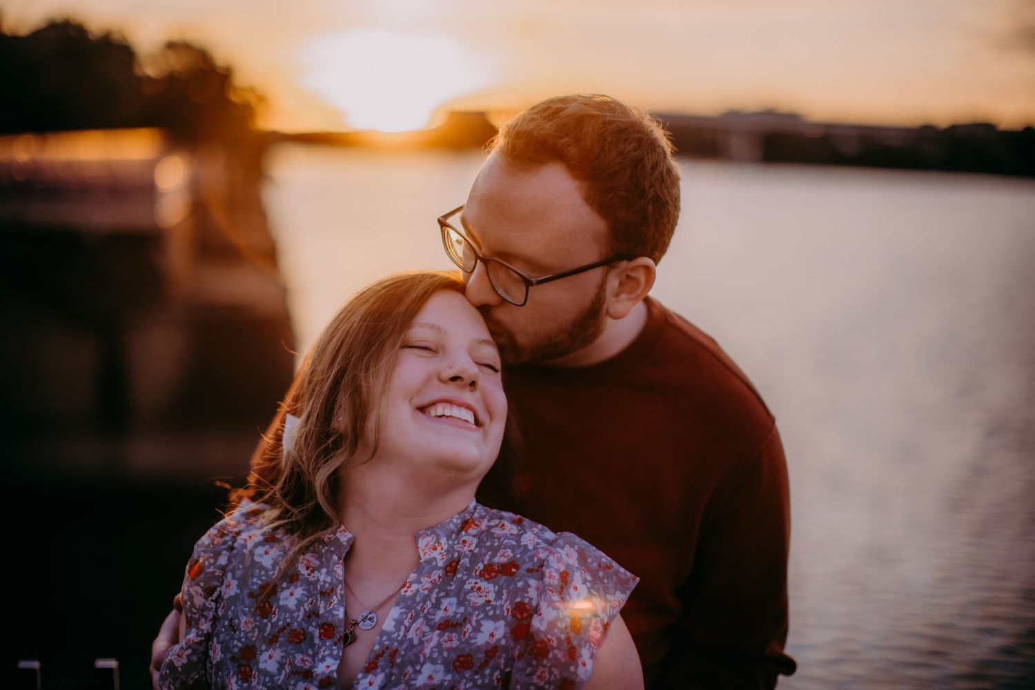 Joyful moment between couple against warm sunset backdrop near water.