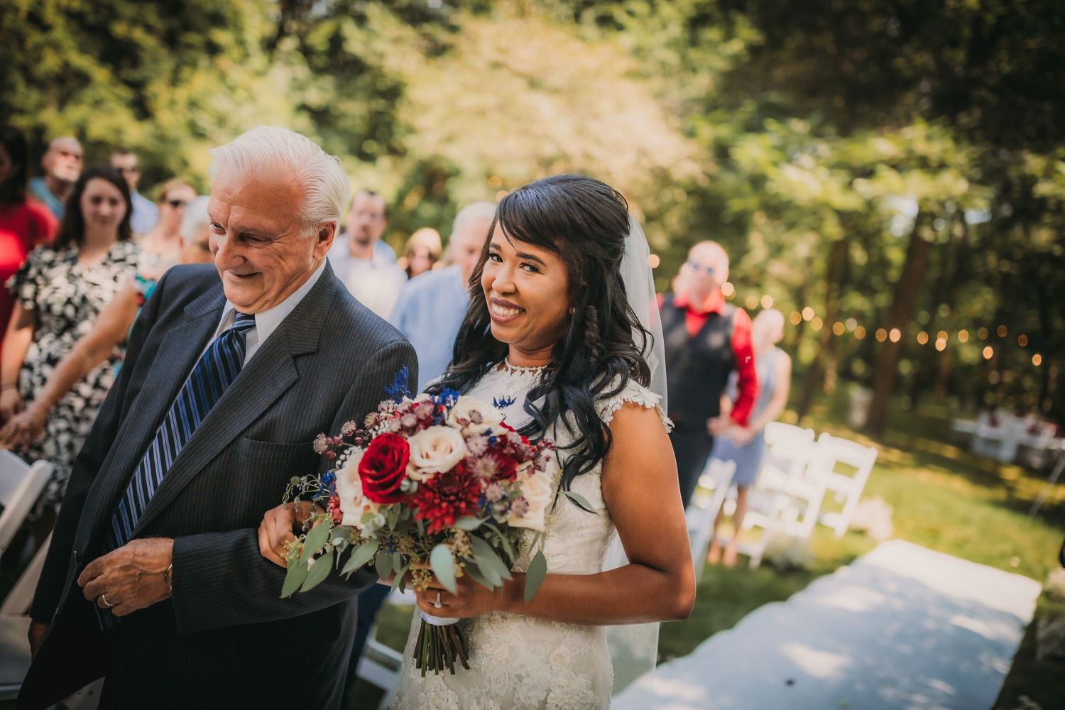 A joyful outdoor wedding ceremony takes place in a lush garden setting with guests seated on white chairs.