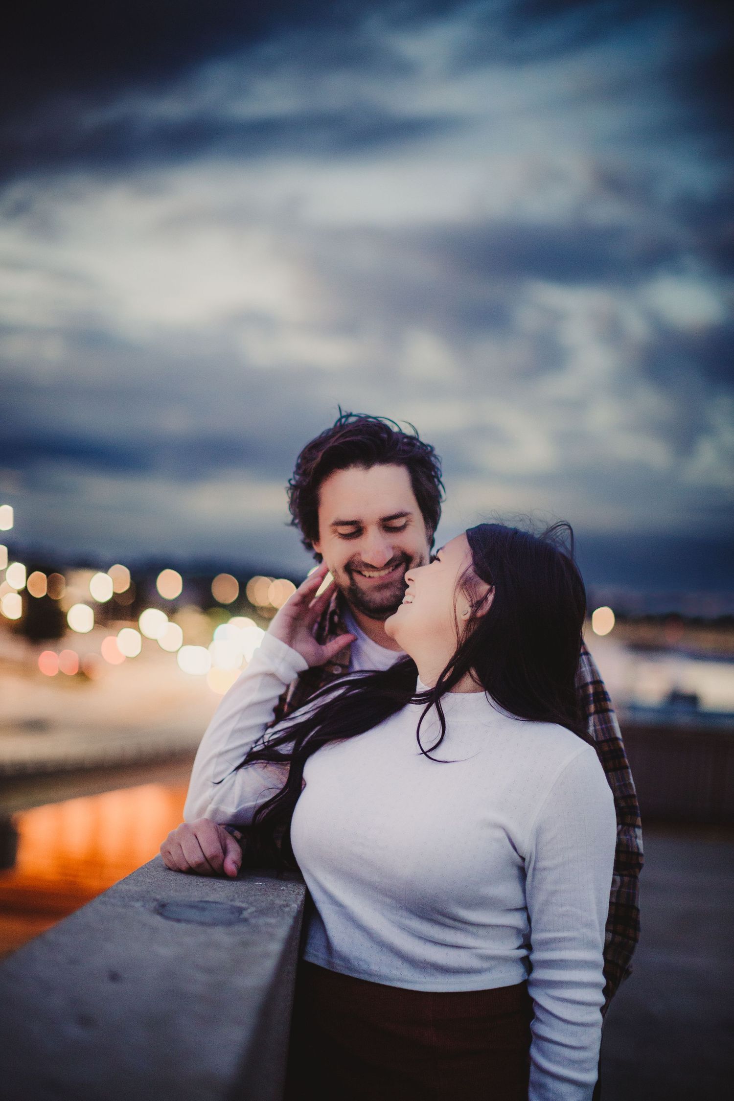 A couple shares a joyful moment together against a twilight cityscape.