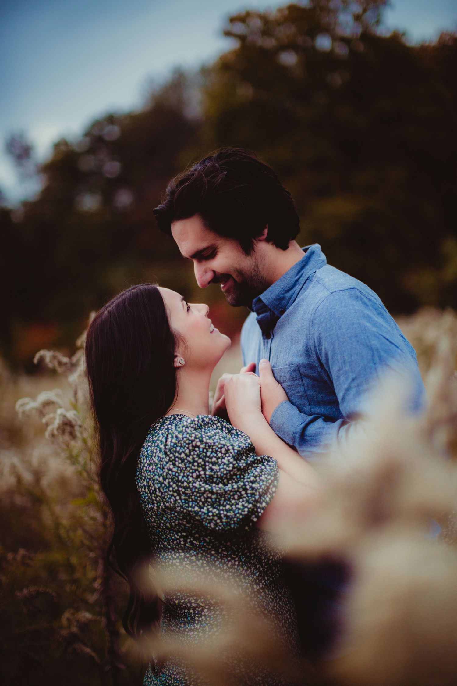 Romantic couple sharing an intimate moment in a field with tall grass at sunset.