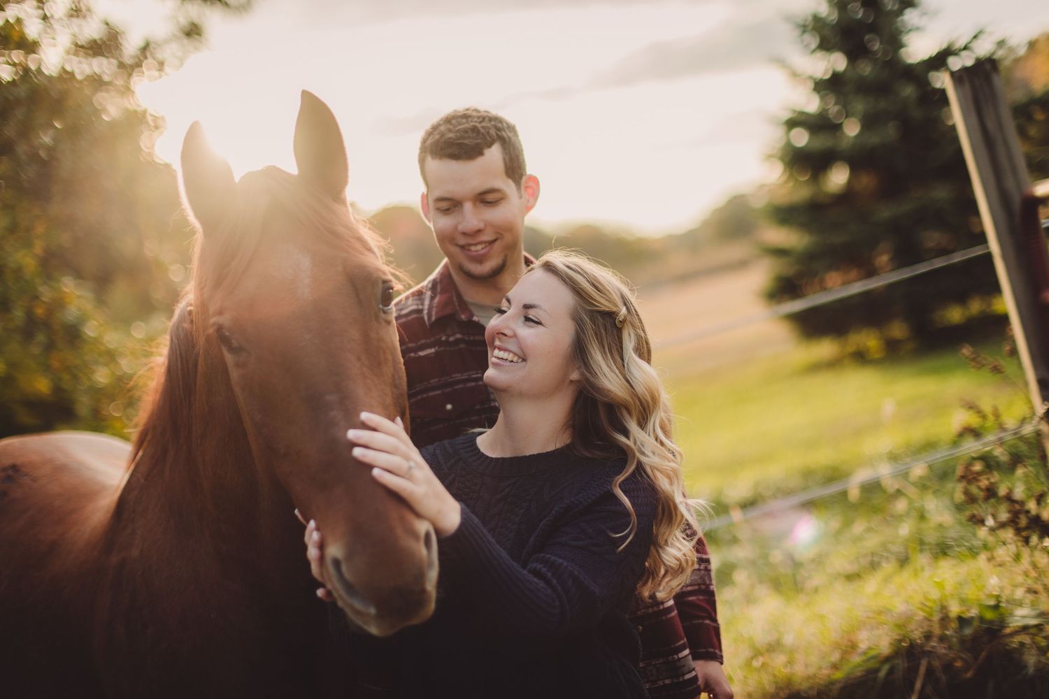 Couple interacts with friendly horse during golden hour photoshoot in countryside.