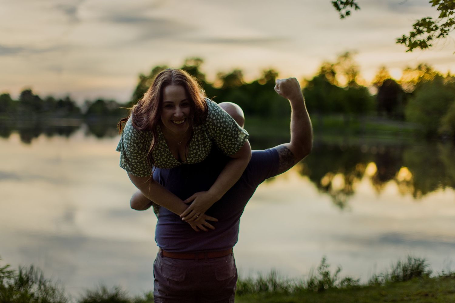 Two people embrace and laugh together near a sunset-lit lake.