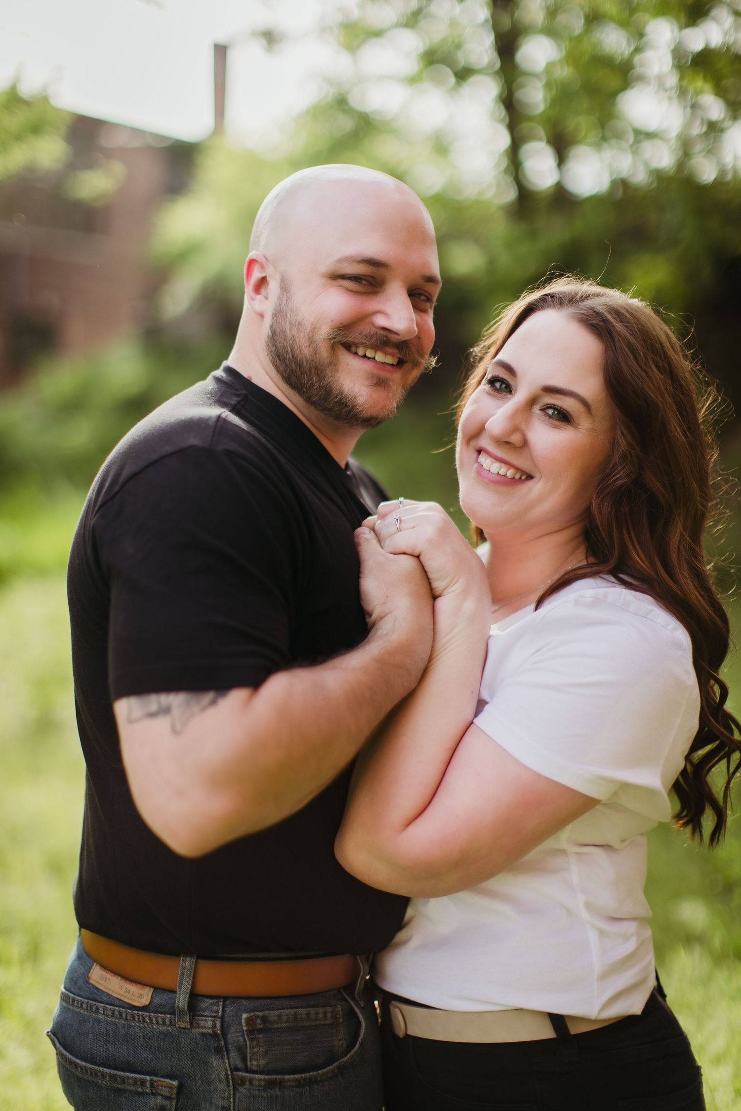 Candid engagement photography showing joyful couple embracing outdoors in natural light.