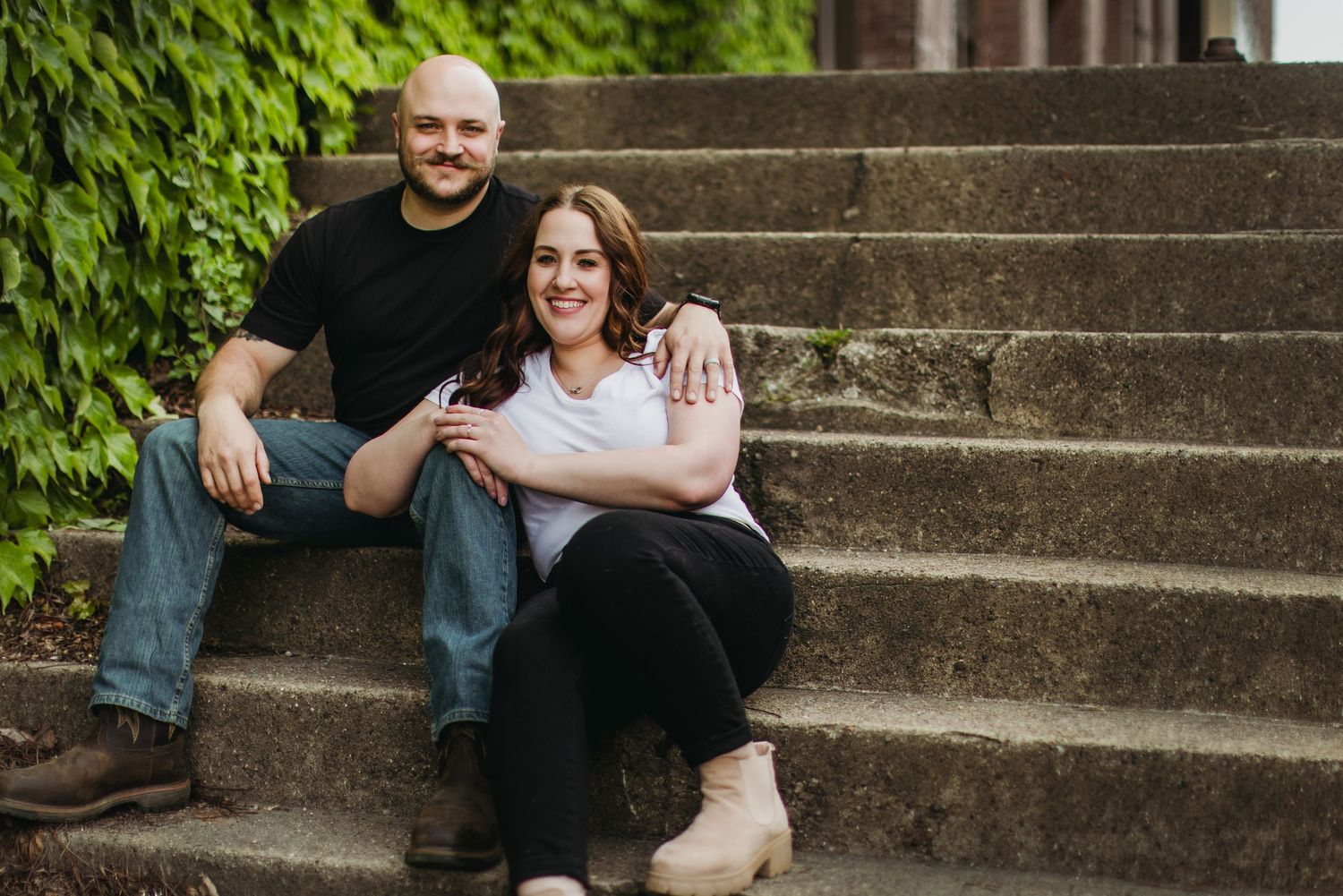Couple sitting together on concrete steps with ivy covered walls in background.