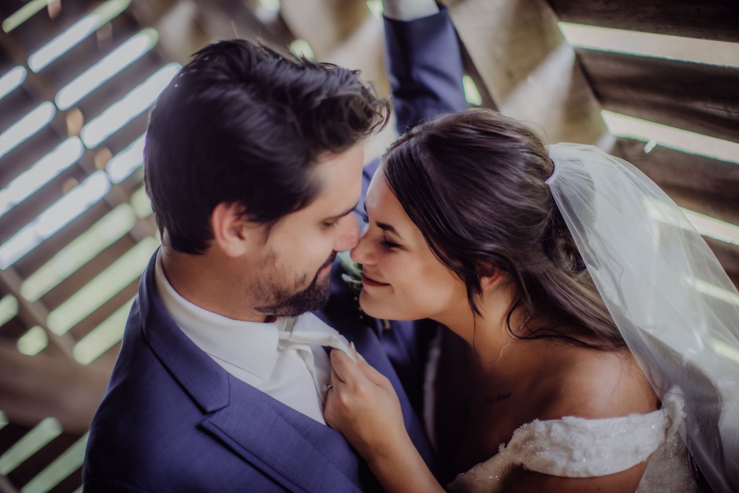 Joyful wedding couple sharing a loving moment against wooden architectural details.