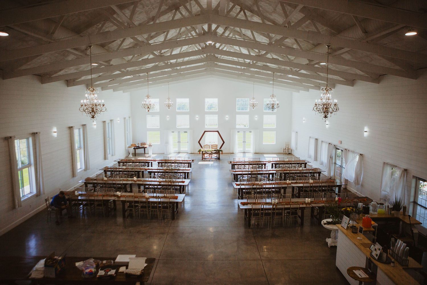 Empty wedding ceremony venue with wooden benches and vaulted ceiling with chandeliers.