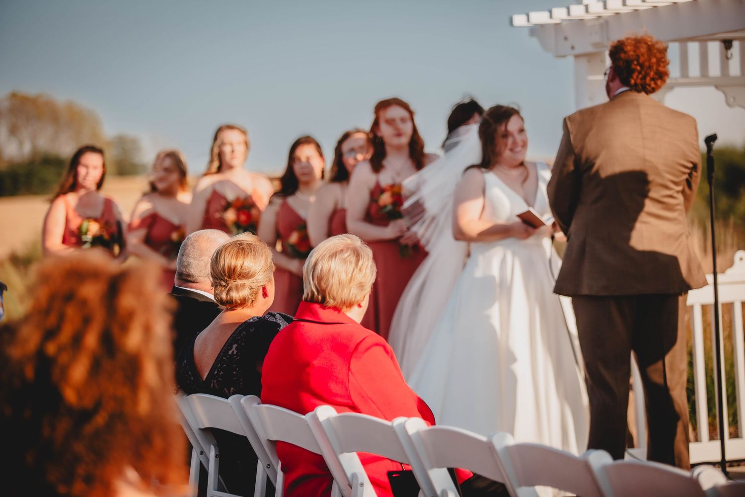 Wedding party in burgundy dresses and white gown gathered under a pergola.