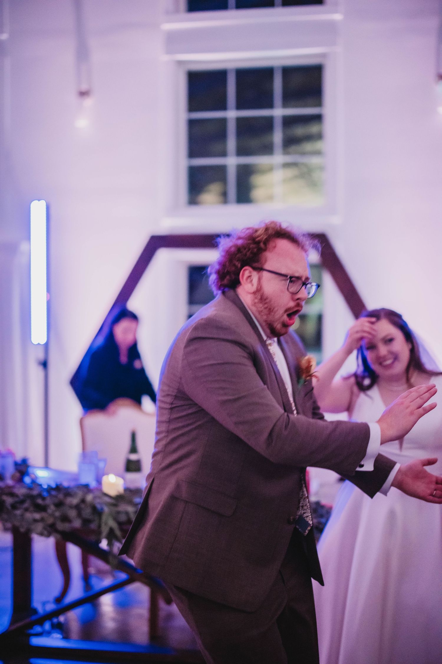 A guest in a suit jacket enthusiastically dances at a wedding reception.