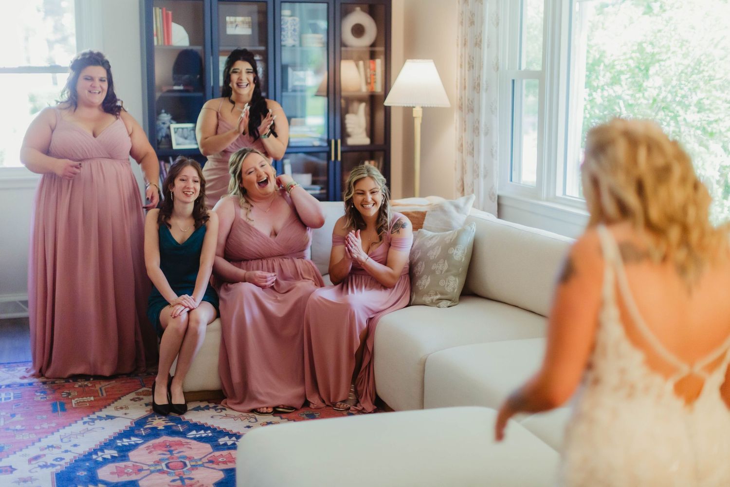 A wedding party shares laughs together in a cozy indoor setting with natural lighting.