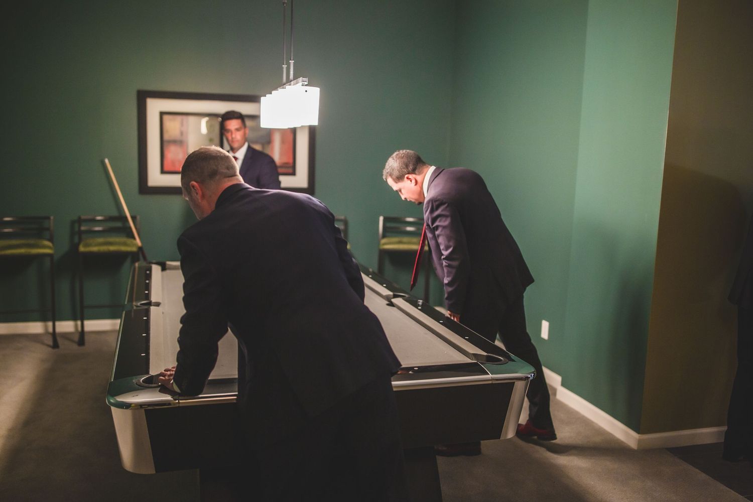 Group playing pool in a room with sage green walls and pendant lighting.