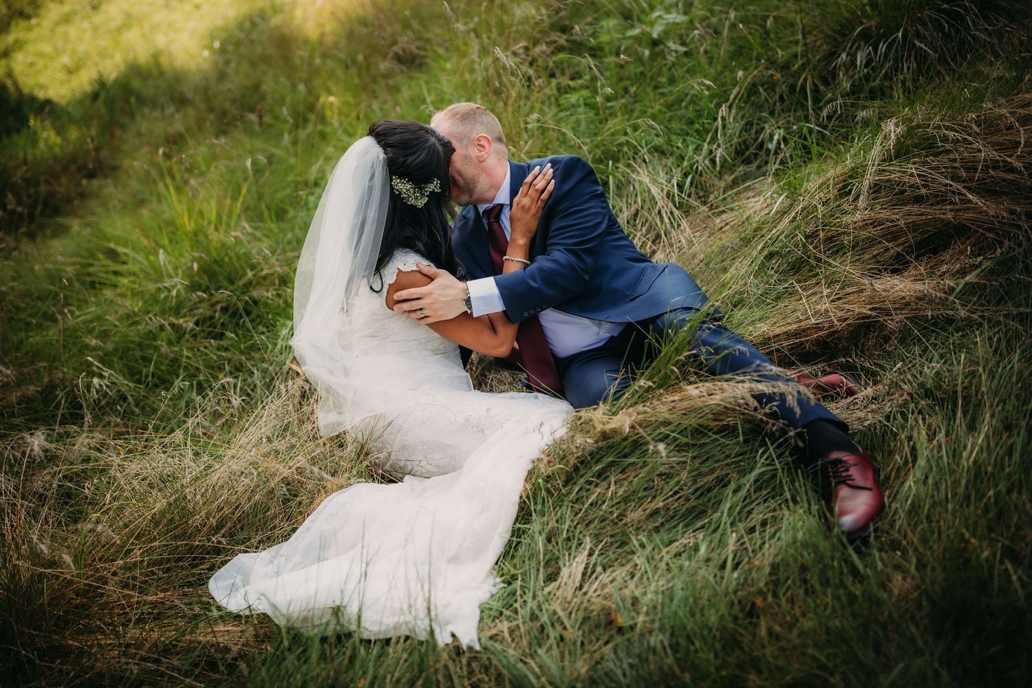 Romantic wedding photo showing couple embracing in tall grass with natural lighting.