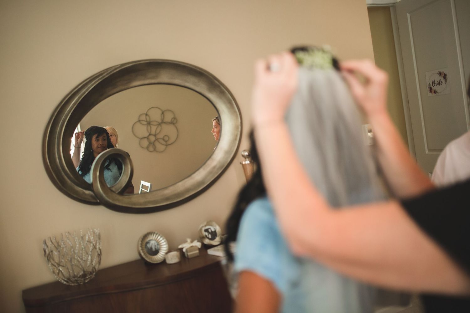 Reflection in oval mirror shows styling session with veil being placed.