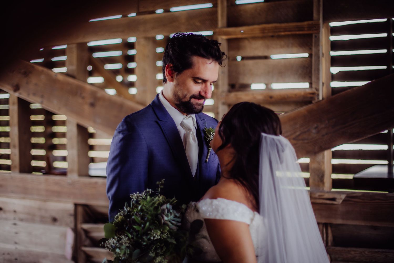Intimate wedding first look sequence with greenery bouquet in rustic barn setting.