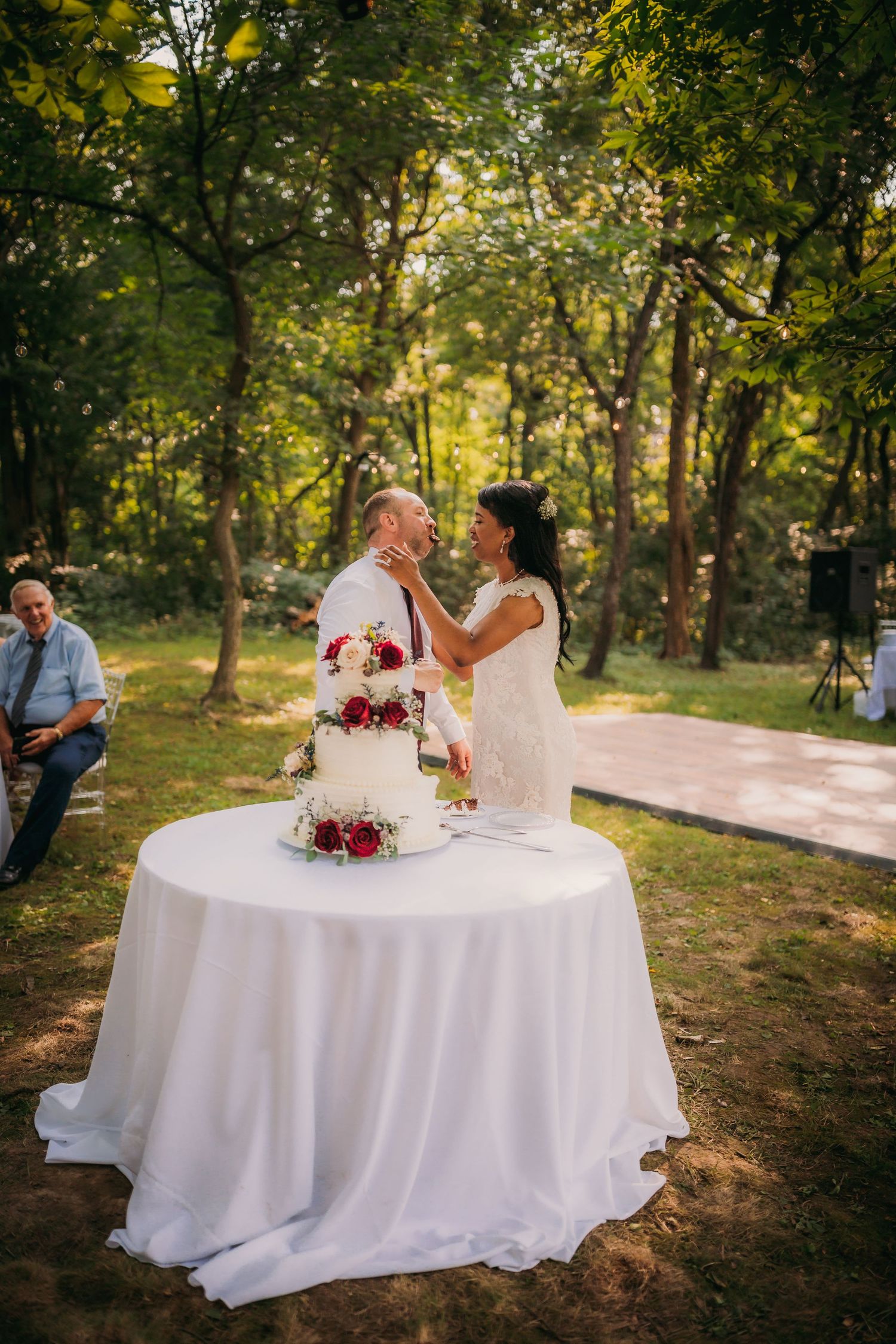 Romantic outdoor wedding scene with couple signing documents beside a decorated white cake.